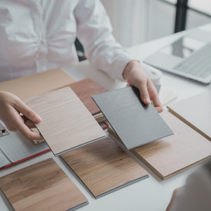 Person holding and comparing different wood sample boards on a desk.
